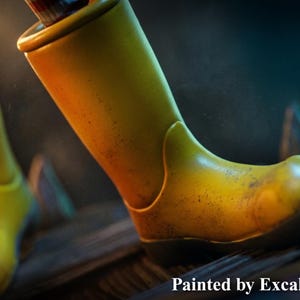 May include: Close-up of two yellow boots with a worn, textured appearance. The boots are set against a dark background, with the text "Painted by ExcaliburCreations" at the bottom. The boots appear to be made of a durable material.