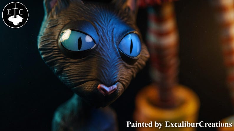 May include: A close-up of a black cat sculpture with large, bright blue eyes and a pink nose. The sculpture is painted by ExcaliburCreations. The cat's fur appears textured, and the background is dark, highlighting the cat's features.