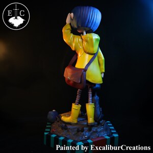 May include: A figurine of a character from the animated film, wearing a yellow raincoat, boots, and a brown satchel. The figure has blue hair and is standing on a detailed base. The text "Painted by ExcaliburCreations" is at the bottom.