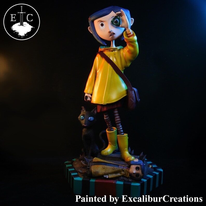May include: A figurine of a girl in a yellow raincoat and boots, holding a green marble eye. A black cat with blue eyes sits beside her. The base is striped with a figure lying down. The text "Painted by ExcaliburCreations" is at the bottom.