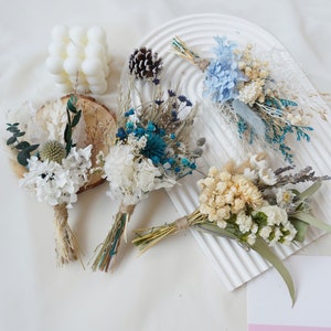 May include: Five small bouquets of dried flowers in various shades of blue, white, and cream. The bouquets are tied with twine and feature dried grasses and eucalyptus.