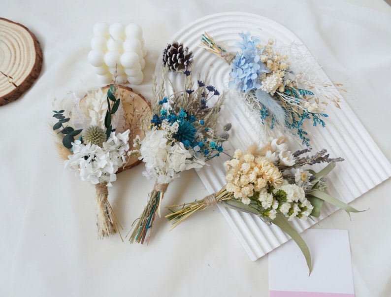 May include: Five small bouquets of dried flowers in various shades of blue, white, and cream. The bouquets are tied with twine and feature dried grasses and eucalyptus.