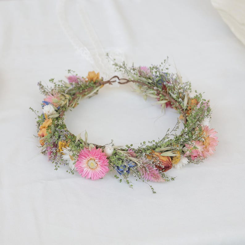 May include: A handmade floral crown featuring a variety of dried flowers in shades of pink, yellow, and blue. The crown is made with a natural twig base and delicate greenery, perfect for a bohemian or rustic aesthetic.
