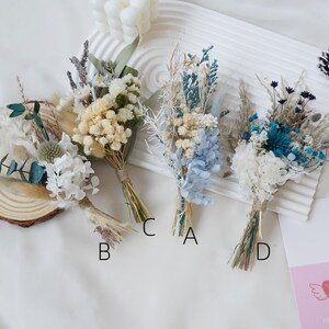 May include: Four small bouquets of dried flowers, each tied with twine. The bouquets are arranged in a row on a white surface. The bouquets are labeled A, B, C, and D. The bouquets are made up of dried flowers in shades of white, blue, and green.