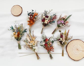 May include: Assortment of eight small bouquets of dried flowers in various colors, including orange, red, pink, and white. The bouquets are tied with twine and arranged on a white surface.