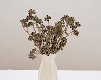 Peut inclure: Un vase en céramique blanc à motif cannelé contient un bouquet de branches d'eucalyptus séchées avec des capsules de graines brunes.