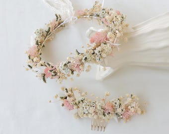 May include: A floral crown and matching hair comb featuring dried flowers in shades of pink, cream, and green. The crown has a lace tie, and the comb has a gold-colored metal base. Perfect for weddings or special occasions.