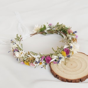 May include: A floral crown made with dried flowers in shades of white, pink, purple, and yellow. The crown is made with a wire base and is decorated with a variety of dried flowers, including daisies, lavender, and wildflowers.