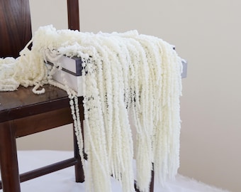 May include: White fluffy garland draped over a wooden chair. The garland is made of long strands of white fluffy material.