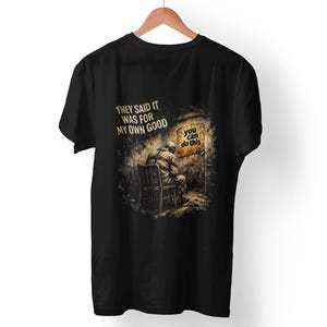 May include: Black t-shirt with a graphic illustration of a person sitting in a dark room. The shirt features the text "THEY SAID IT WAS FOR MY OWN GOOD" and "you can do this."