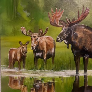 Op de afbeelding: Een olieverfschilderij toont een elandenfamilie in een wetland. Een mannetjeseland met groot gewei, een koe en een kalf staan in ondiep water. Het schilderij gebruikt bruine, groene en blauwe tinten. De reflecties van de elanden in het water zijn zichtbaar.