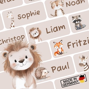Könnte beinhalten: Eine Sammlung illustrierter Namensschilder mit verschiedenen Tieren, darunter ein Löwe, eine Giraffe, ein Fuchs und ein Zebra. Jedes Schild hat einen Namen in brauner Schrift. Die Schilder sind vor einem hellbeigen Hintergrund angeordnet. Der Schriftzug "Made in Germany" ist ebenfalls zu sehen.