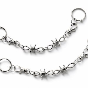 May include: Two silver-colored keychains with a barbed wire design. Each keychain has a ring, a lobster clasp, and a chain with barbed wire accents. The keychains are displayed on a white background.