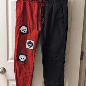 May include: Red and black pants with a tie-dye effect on the black side. The red side has three white skull patches.