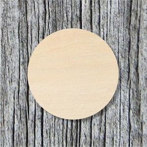 May include: A round, unfinished wooden disc with a light tan color. The disc is centered against a weathered, gray wooden background. The wood grain is visible on both the disc and the background.