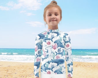 May include: A white long-sleeved shirt with a colorful print of hammerhead sharks, whale sharks, and coral reefs. The shirt is perfect for a day at the beach or pool.