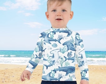 May include: A white long-sleeved shirt with a blue and white pattern of sharks and other sea creatures. The shirt is made of a soft, comfortable material and is perfect for swimming or playing in the water.
