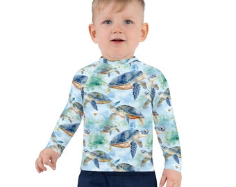 May include: A light blue long-sleeved shirt with a watercolor pattern of sea turtles swimming in the ocean. The shirt has a mock neck and is made of a soft, comfortable material.