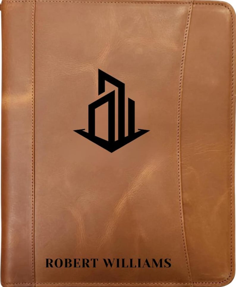 May include: A brown leather portfolio with a black architectural logo and the name "ROBERT WILLIAMS" printed at the bottom. The portfolio has a stitched border and a vertical seam on the right side.