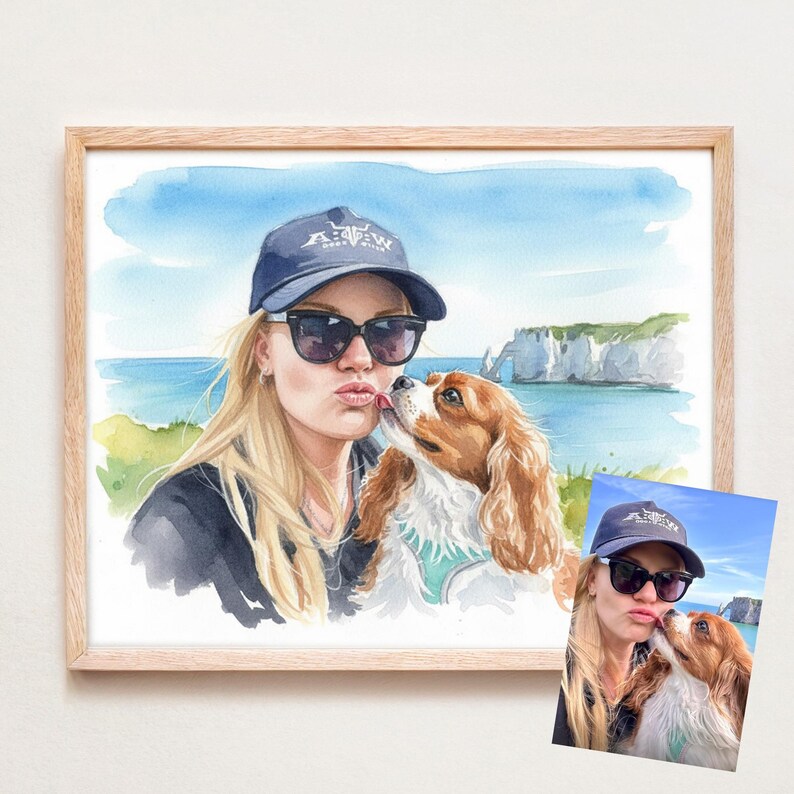 May include: Watercolor portrait of a person and a Cavalier King Charles Spaniel dog, framed in a light wood. The person wears sunglasses and a navy blue cap with white text. The dog has brown and white fur.