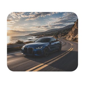 May include: A blue sports car speeds along a coastal highway, with the ocean and mountains in the background. The car is dark blue with black wheels. The sky is a mix of blue and orange, suggesting a sunset or sunrise.