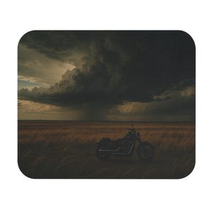 May include: A mousepad featuring a dramatic landscape with a motorcycle parked in a field of tall grass under a stormy sky. The image has a dark, moody aesthetic with a focus on the motorcycle.