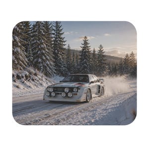 May include: A white Audi rally car with prominent circular front fog lights and black and red racing decals driving on a snow-covered road. The vehicle features a wide body kit and a rear spoiler, kicking up snow dust against a backdrop of pine trees.