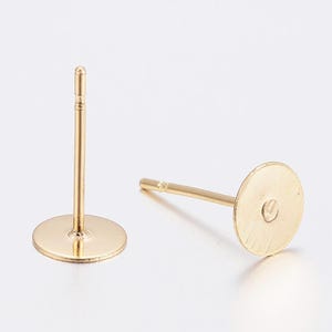 May include: Two gold-coloured earring posts with flat, round pads. One post is upright, showing the full length of the post and pad. The other post is lying down, showing the back of the pad and the post's details. These are jewellery making supplies.