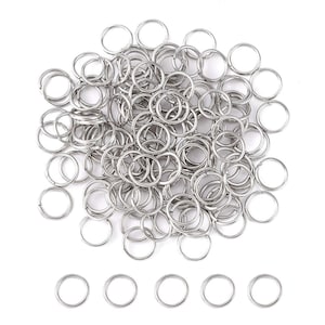 May include: A large pile of silver jump rings, with a row of six smaller jump rings below. These rings are used for jewelry making and crafting.