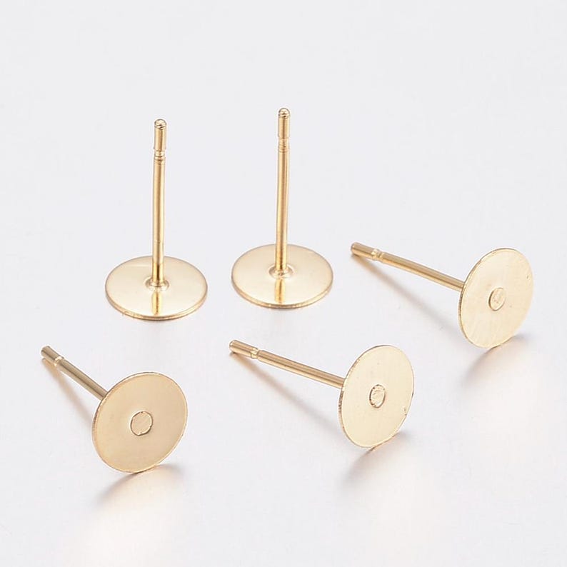May include: Several gold-coloured earring posts with flat, round pads. The posts are straight with a small, rounded tip. The pads have a small hole in the centre for attaching earrings. Suitable for DIY jewellery making.