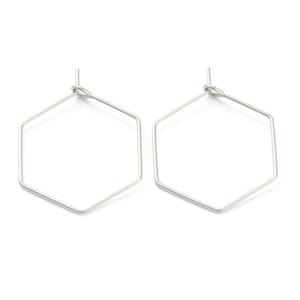 以下が含まれることがあります： シルバーカラーの幾何学的な六角形のフープピアス。ピアスは細い金属線で作られており、シンプルでモダンなデザインです。フープは上部で小さなループで接続されています。