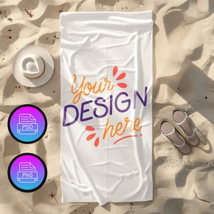 Op de afbeelding: Wit strandlaken met de tekst "Your Design Here" in paarse en oranje letters op een zandstrand.