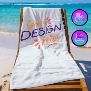 Op de afbeelding: Wit strandlaken met de tekst "Your Design Here" in paarse, oranje en roze letters. De handdoek is gevouwen en op een houten strandstoel geplaatst.