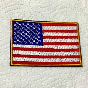 May include: A small embroidered American flag patch with a gold border. The flag is red, white, and blue with white stars on a blue field.