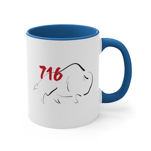 Op de afbeelding: Witte keramische mok met een blauwe binnenkant en handvat. De mok heeft een zwarte lijntekening van een bizon en het nummer "716" in rood. De mok is een standaard maat voor koffie of thee.