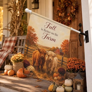 Puede incluir: Una bandera de jardín rectangular que muestra dos vacas Highland en un campo con un granero rojo al fondo. El texto "Fall is Better on the Farm" está impreso en letra cursiva marrón. La bandera está montada en un soporte de metal blanco.