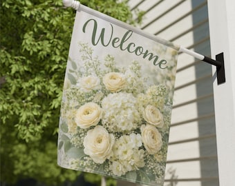 May include: A decorative outdoor flag with the word "Welcome" in green script. The flag features a floral design with cream-colored roses and other white flowers. The flag is mounted on a white pole and black bracket.