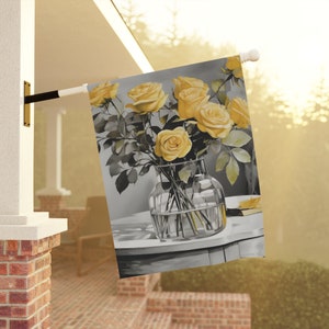 May include: A grey and yellow garden flag featuring a bouquet of yellow roses in a clear glass vase. The roses are arranged in a vase on a grey table.