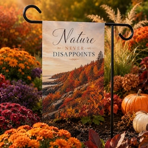 May include: A rectangular garden flag hanging on a black metal stand, featuring a scenic autumn landscape with orange and red trees along a rocky coastline. The text Nature NEVER DISAPPOINTS is printed in black and brown script and serif fonts.