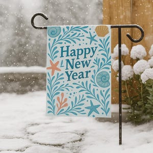 May include: A garden flag with the text "Happy New Year" in blue, surrounded by teal and coral sea-themed illustrations. The flag is displayed on a black metal stand in a snowy outdoor setting.