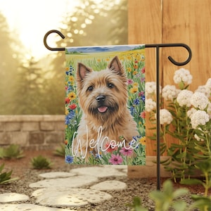 May include: A welcome garden flag featuring a Cairn Terrier dog with brown fur standing in a field of colorful flowers. The text "Welcome" is written in white cursive lettering.