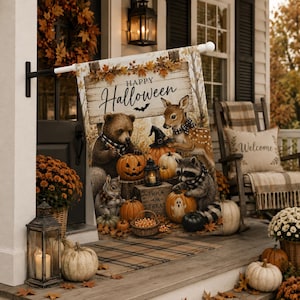 Puede incluir: Una bandera de jardín rectangular con un letrero de madera que dice Happy Halloween. La ilustración muestra un oso, un ciervo, una ardilla y un mapache rodeados de calabazas, una linterna y una cesta de dulces sobre una superficie de madera.