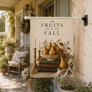 May include: A rectangular garden flag featuring the text The FRUITS of FALL above a bowl of pears, two brass candlesticks with lit candles, and a stack of three vintage books. The design includes autumn foliage and a draped beige fabric cloth.