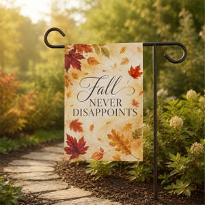 May include: A rectangular garden flag hanging on a black metal stand, featuring a cream-colored background with scattered watercolor autumn leaves in shades of red, orange, and yellow. The text "Fall NEVER DISAPPOINTS" is printed in black.