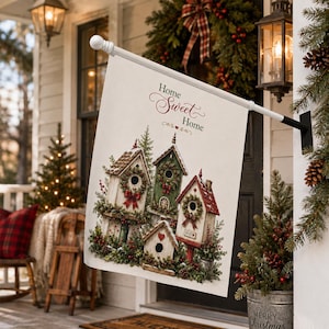May include: A cream-coloured garden flag featuring the text Home Sweet Home and an illustration of four wooden birdhouses decorated with evergreen wreaths, red bows, and snow, hanging from a white metal pole mounted on a porch wall.
