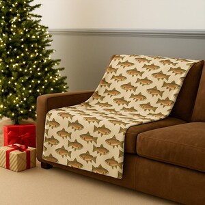May include: A beige throw blanket draped over a brown sofa, featuring a repeating pattern of brown fish. The blanket is made of a soft material and adds a decorative touch to the living room.