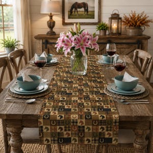 May include: A rectangular table runner featuring a repeating patchwork pattern of brown, black, and tan plaid squares interspersed with silhouettes of horse heads and horseshoes, centered on a wooden dining table with place settings.