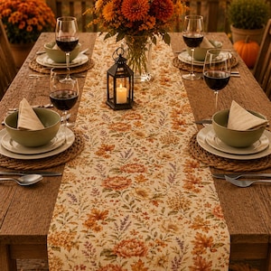 Peut inclure: Un chemin de table rectangulaire orné d'un motif floral répétitif aux tons automnaux orange, rouille et marron sur fond crème. Le chemin de table est disposé au centre d'une table en bois avec des bols verts, des verres à vin et une lanterne.