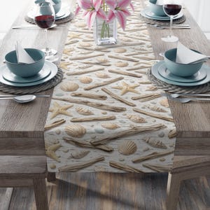 May include: A coastal-themed table runner featuring a pattern of seashells, driftwood, and starfish on a white wood-grain background. The runner is displayed on a wooden table set with teal-colored bowls, plates, and wine glasses, creating a beachy dining aesthetic.
