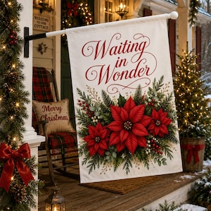 May include: A white rectangular garden flag featuring the red script text Waiting in Wonder above a vibrant illustration of red poinsettia flowers, green pine branches, and small white berries, suspended from a black metal pole on a porch.